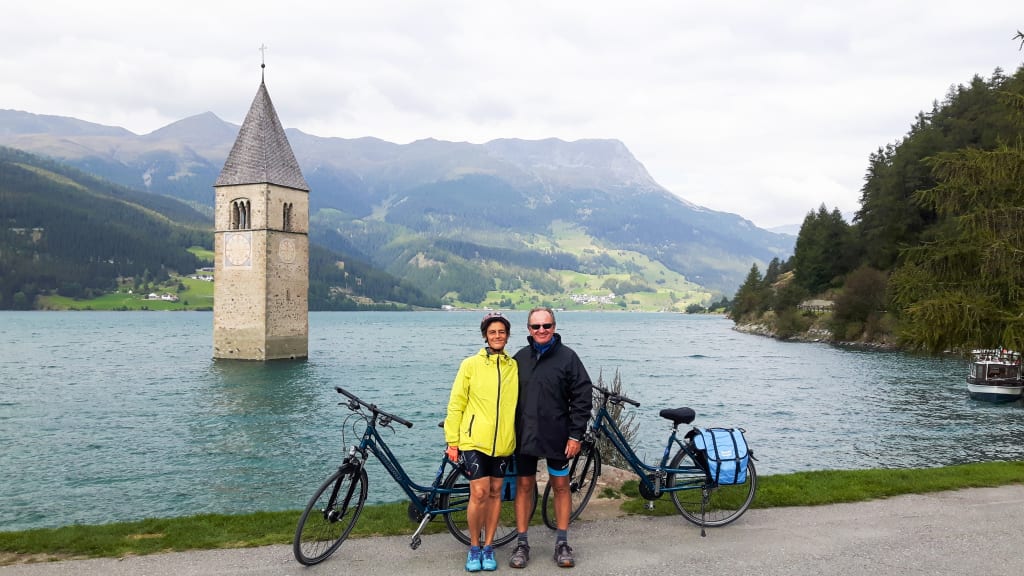 Cyclists next to the submerged bell tower in Lake Resia, South Tyrol, Italy.